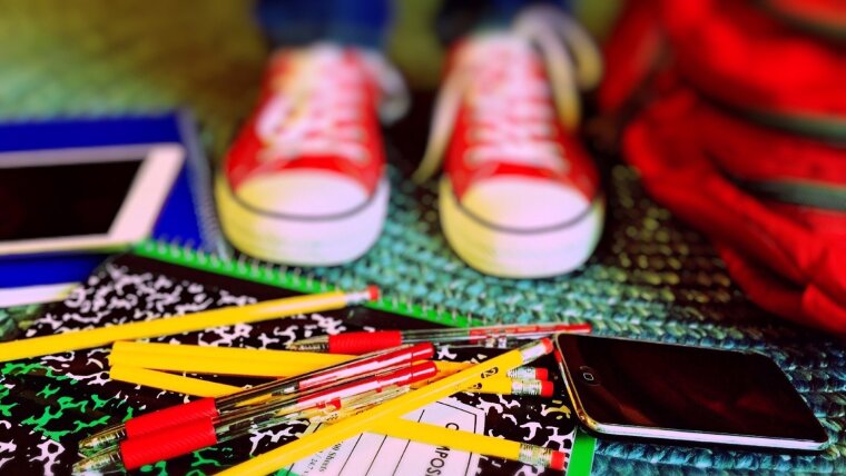 Rote Turnschuhe stehen hinter Schulsachen und Handy