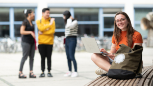 Eine junge Studentin sitzt auf dem Campus am Laptop