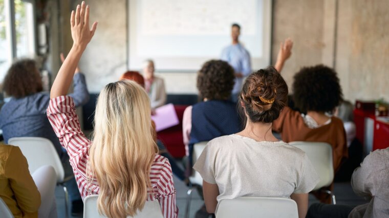 Junge Menschen sehen sich eine Präsentation an und heben die Hand für eine Frage