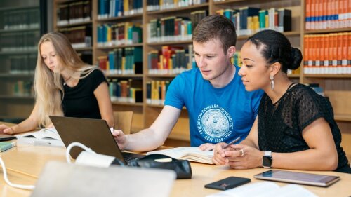 Studierende sitzen vor Laptop in Bibliothek