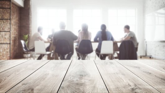 Gruppe Personen sitzt zusammen, Holztisch im Vordergrund