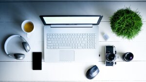 Laptop, Kaffee, Kamera, Pflanze, Telefon und Kopfhörer auf einem Tisch